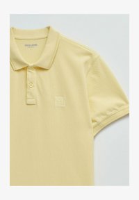 Polo de manga corta color amarillo claro con dos botones, cuello y logo en relieve de "Salsa Jeans" en el pecho.