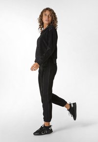 Schwarzer, kurzer Sweatshirt aus einem strukturierten Stoff, kombiniert mit einer schwarzen Hose mit kontrastierenden Seitenstichen und elastischen Bündchen, getragen mit schwarzen Turnschuhen.