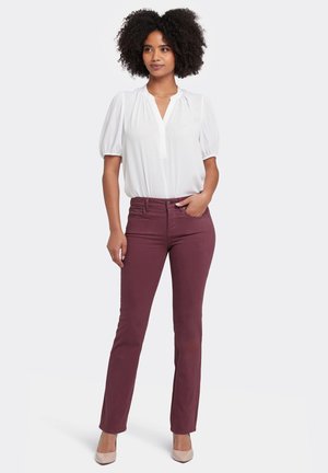 Witte blouse met korte mouwen, een V-hals en geplooide schouderdetails, gecombineerd met bordeauxkleurige skinny jeans en naaldhakken in huidskleur.