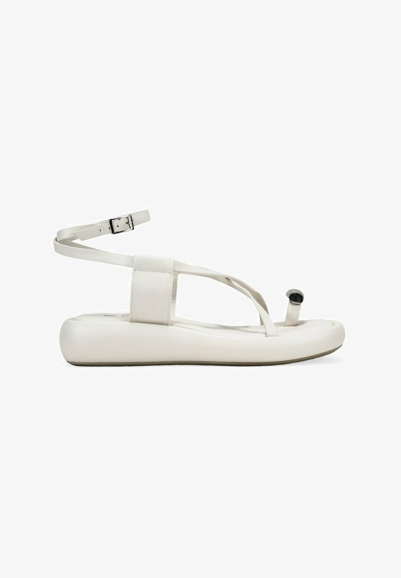 Sandal flat bianco con cinturino alla caviglia, caratterizzata da una superficie liscia simile alla pelle, design minimalista e un piccolo accento nero sul sostegno dell'alluce.