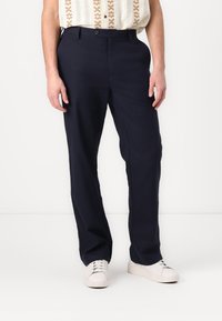 Marineblauwe broek vervaardigd uit lichtgewicht stof, met een knoopsluiting, rechte pasvorm en minimalistische stijl. Witte sneakers maken de look compleet.