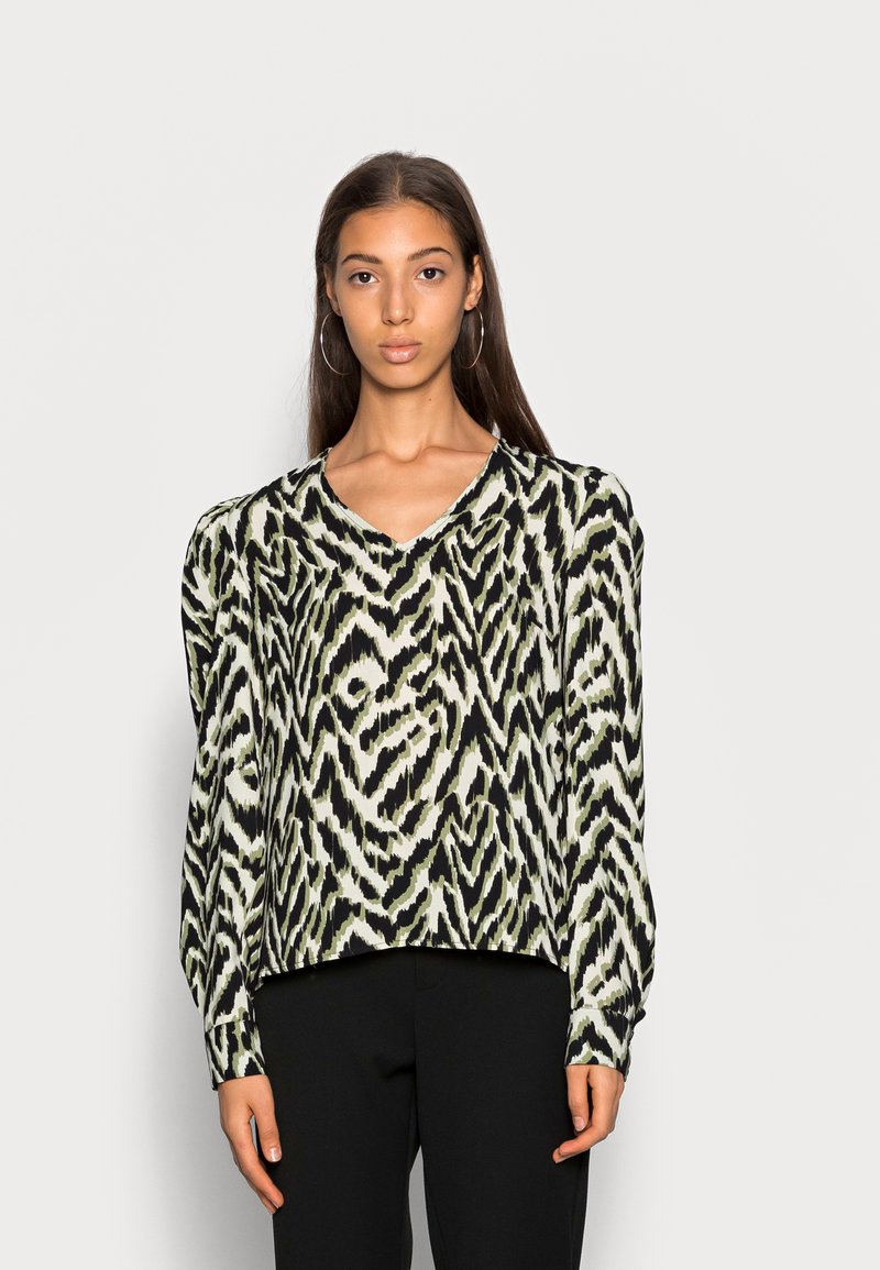 Blusa de mangas longas com um padrão zigzag verde e preto, decote em V e tecido suave. Ajuste entalhado com detalhes franzidos nos ombros.