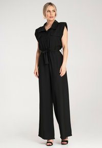 Czarny kombinezon z krótkimi, strukturalnymi rękawami, z przodu zapinany na guziki, z paskiem w talii i szerokimi nogawkami, uszyty z gładkiego materiału.