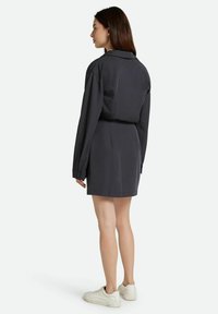 Dunkelgraues Hemdkleid mit langen Ärmeln, einem Kragen und einer taillierten Passform. Weiche Textur, kombiniert mit hellen Sneakers.