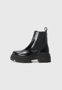 Bottines en cuir noir à la conception élégante, avec panneaux élastiques sur les côtés et une semelle épaisse noire. Dotées d'une tirette à l'arrière pour un enfilage facile.