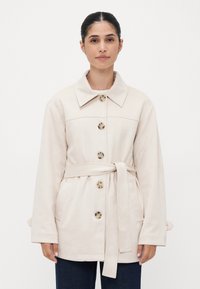 Beige belted coat with a notched collar, five round buttons, and two side pockets, featuring a smooth texture and relaxed fit.