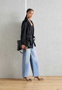 Blazer negro, top ajustado negro, vaqueros de pierna ancha de lavado claro y tacones altos con estampado de leopardo. Bolso negro con detalle de cadena. Texturas suaves.