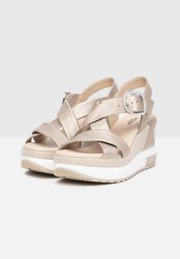 Beige wedge sandals with cross straps, metallic finish, adjustable buckle, and textured detailing on the heel; lightweight white sole.