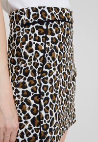 Falda de estampado de leopardo con manchas negras y marrones sobre un fondo blanco. Tela texturizada, diseño ajustado y detalles en los paneles laterales son visibles.