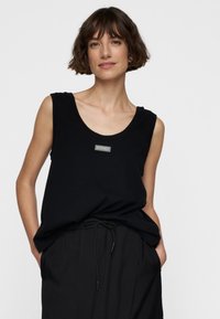 Zwarte mouwloze top van zachte katoen met een ronde halslijn en een klein logo-opstikke. Gecombineerd met loszittende zwarte broeken met een elastische trekkoord.