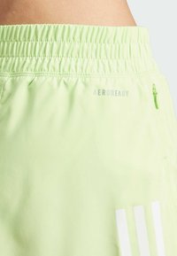 Light green AEROREADY athletic shorts with elastic waistband, reflective logo, and side zipper pocket. Smooth, breathable fabric texture.