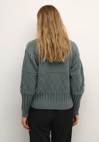 Maglione lavorato a maglia in un verde teal tenue con motivi a diamante e a coste, caratterizzato da una vestibilità rilassata e maniche lunghe.
