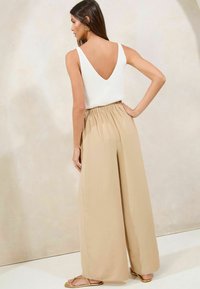 Débardeur blanc à côtes avec un dos en V profond, associé à un pantalon ample beige taille haute, présentant une finition texturée et une taille froncée.