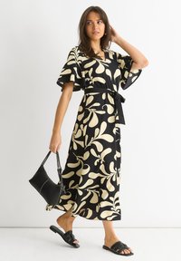 Musta ja kerma värinen kukkakuosiset mekko, jossa on lyhyet röyhelöhiat, vyötärö on kireä ja siluetti soljuva. Mekko on yhdistetty mustiin sandaaleihin ja käsilaukkuun.