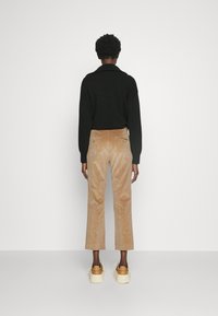 Suéter negro de punto con cuello vuelto, combinado con pantalones cortos de pana marrón claro y zapatillas de plataforma beige. Textura suave, detalles mínimos.