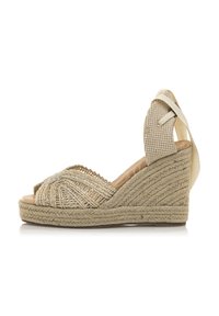 Sandale compensée en espadrille beige avec un dessus en textile tissé, bout ouvert et sangle à la cheville. Les détails en jute le long de la semelle ajoutent de la texture.