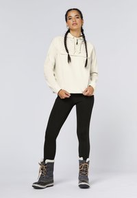 Beige zip-up pullover with a front pocket, black leggings, and gray waterproof winter boots with fur lining and lace-ups.
