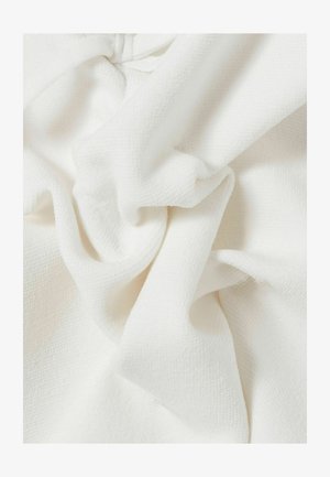 Tela blanca suave y texturizada con pliegues irregulares y sombras suaves, que resaltan su material esponjoso y ligero.