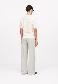 Jasnoszare spodnie o szerokich nogawkach z miękkiego materiału, połączone z krótkim, off-white topem uszytym z gładkiego, lekkiego materiału.