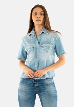 Helles blaues Denim-Hemd mit kurzen Ärmeln, das über zwei Brusttaschen, Druckknöpfe und ein leicht abgenutztes Finish mit klassischem Kragen verfügt.