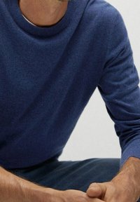 Suéter azul de cuello redondo hecho de material suave, con un cuello acanalado y mangas largas, combinado con pantalones azul marino.