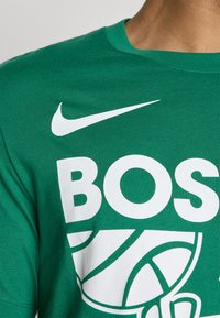 Zielona bawełniana koszulka z okrągłym dekoltem, z białym logo Nike oraz dużym białym napisem "BOSTON" obok grafiki koszykówki.