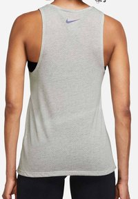 Hellgraues sportliches Tanktop mit strukturierter Mesh-Optik, lila Nike-Logo in der Nähe des Ausschnitts und lockerer Passform.