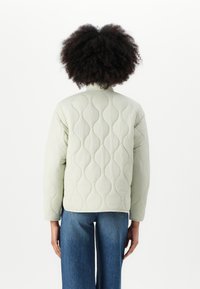 Lichtgroen gewatteerd jack met een ronde halslijn, voorzien van een golvenpatroon en lange mouwen, gecombineerd met blauwe wijde jeans.