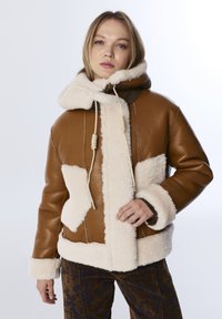 Bruine leren jas met crèmekleurige fleece accenten, een capuchon en trekkoorddetails. Heeft een boxy silhouet en textuurpatronen op de stof.