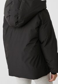 Schwarze Pufferjacke mit Kapuze, mit einer weichen Textur und einem leicht übergroßen Design. Der Rücken ist glatt mit minimalen Nähten.