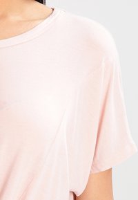 Kortärmad t-shirt med rund hals i ljusrosa, tillverkad av mjukt tyg, med avslappnad passform och subtil textur på ytan.