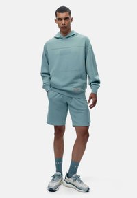 Hele sinine kapuutsiga särk, millel on ees tasku, koos sobivate lühikesed pükste ja pehme puuvillase kangaga ning lihtsa disainiga. Komplekti kuuluvad ka helesinised tennisetossud.