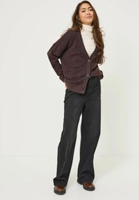 Gilet bordeaux avec un col en V, doté de boutons sur le devant et de manches longues, associé à un pantalon large noir et des chaussures marron.