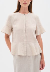 Beige lněný peplum top s krátkými rozšířenými rukávy a knoflíkovým zapínáním na výstřihu. Má texturovanou látku s jemným leskem.