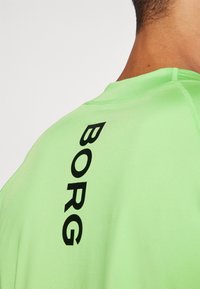 Neon zöld sportpóló kör alakú nyakkivágással. A hátsó részen fekete "BORG" felirat látható függőlegesen. Simább anyagú, rövid ujjú.
