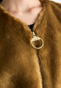 Braune gefälschte Pelzjacke mit V-Ausschnitt, glatter Textur und einem auffälligen goldfarbenen Reißverschluss-Zieher mit eingraviertem "Barbour"-Logo.