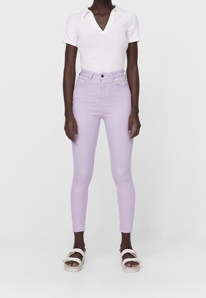 Top blanco de manga corta con cuello, combinado con jeans ajustados lavanda y sandalias blancas con detalles de hebilla.