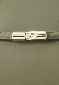 Olivengrüne synthetische Tasche vorne mit glatter Textur und einem goldfarbenen Verschluss mit kreisförmigem Design und eleganten Linien.