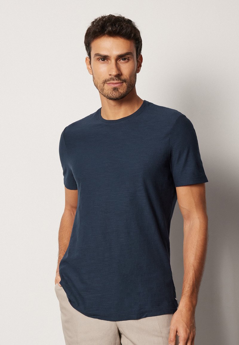 Mörkblå, rundhalsad t-shirt i ett lätt och slätt tyg. Kort ärm och rak fåll. Har subtil textur och ingen synlig logotyp.