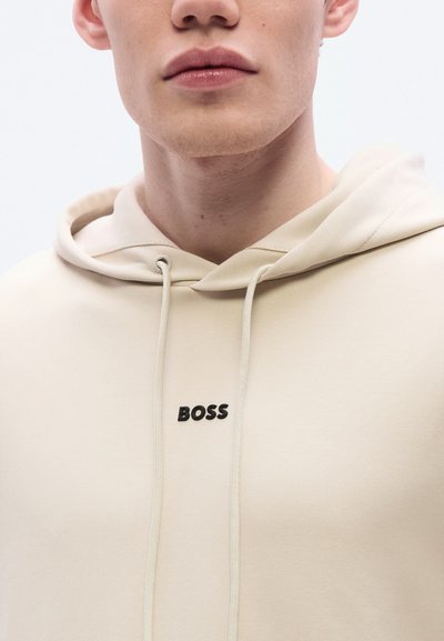 Sweat à capuche beige avec un logo frontal affichant le mot "BOSS" en noir. Il est doté d'une capuche à cordon de serrage et d'une texture lisse et douce.