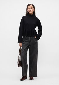 Svart cropped genser med peplum-kant, sammen med høyt liv mørkegrå vide bukser. Tilbehørt med en brun håndveske og hæler.