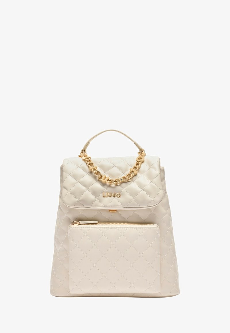 Zaino beige trapuntato con manico a catena dorata e tasca frontale con zip. Presenta una chiusura con patta e logo impresso sul davanti.