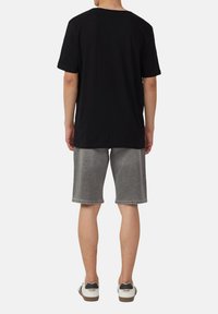 Czarna koszulka z krótkim rękawem, wykonana z miękkiego materiału, w połączeniu z szarymi szortami dżinsowymi i białymi trampkami z szarymi akcentami.