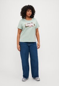 Light green short-sleeve t-shirt with floral print, paired with loose blue jeans and grey athletic shoes. Simple, casual design.