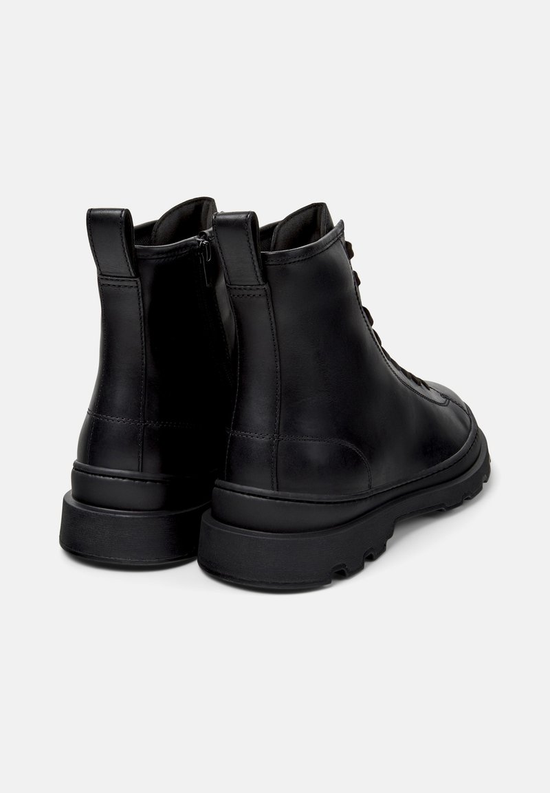 Ein Paar schwarze Lederknöchelstiefel mit Schnürung vorne und seitlichem Reißverschluss, dicke robuste Sohle und Anziehschlaufen hinten, von hinten betrachtet.