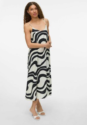 Robe maxi à motifs en vagues noir et blanc avec fines bretelles, fabriquée dans un tissu doux, offrant une coupe décontractée et une longueur mi-mollet.