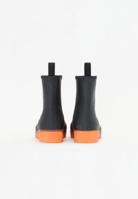 Cizme de glezna negre din cauciuc cu talpă portocalie, având bandă de prindere și o textură netedă. Concepție waterproof și ușor de purtat.