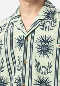 Kortärmad skjorta i ljusgrön med marinblå mönster som har sol- och bladdesign, knappstängning och bröstficka.