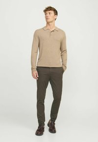 Braunes Langarm-Polohemd mit einer Knopfleiste mit drei Knöpfen, kombiniert mit dunkelgrünen Slim-Fit-Hosen und braunen Schnürschuhen.