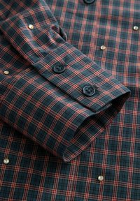 Chemise à carreaux bleue et rouge avec un col boutonné, des boutons noirs et des accents dorés décoratifs sur la surface du tissu.